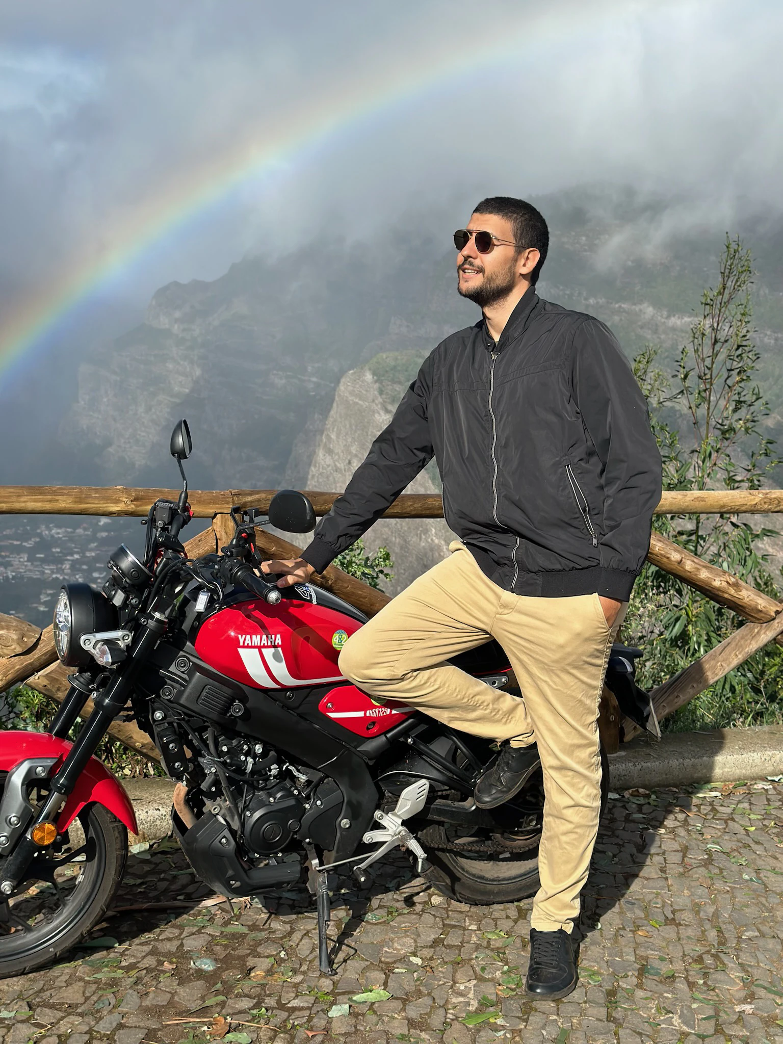 Martin Donadieu auf einem Motorrad mit einem Regenbogen im Hintergrund